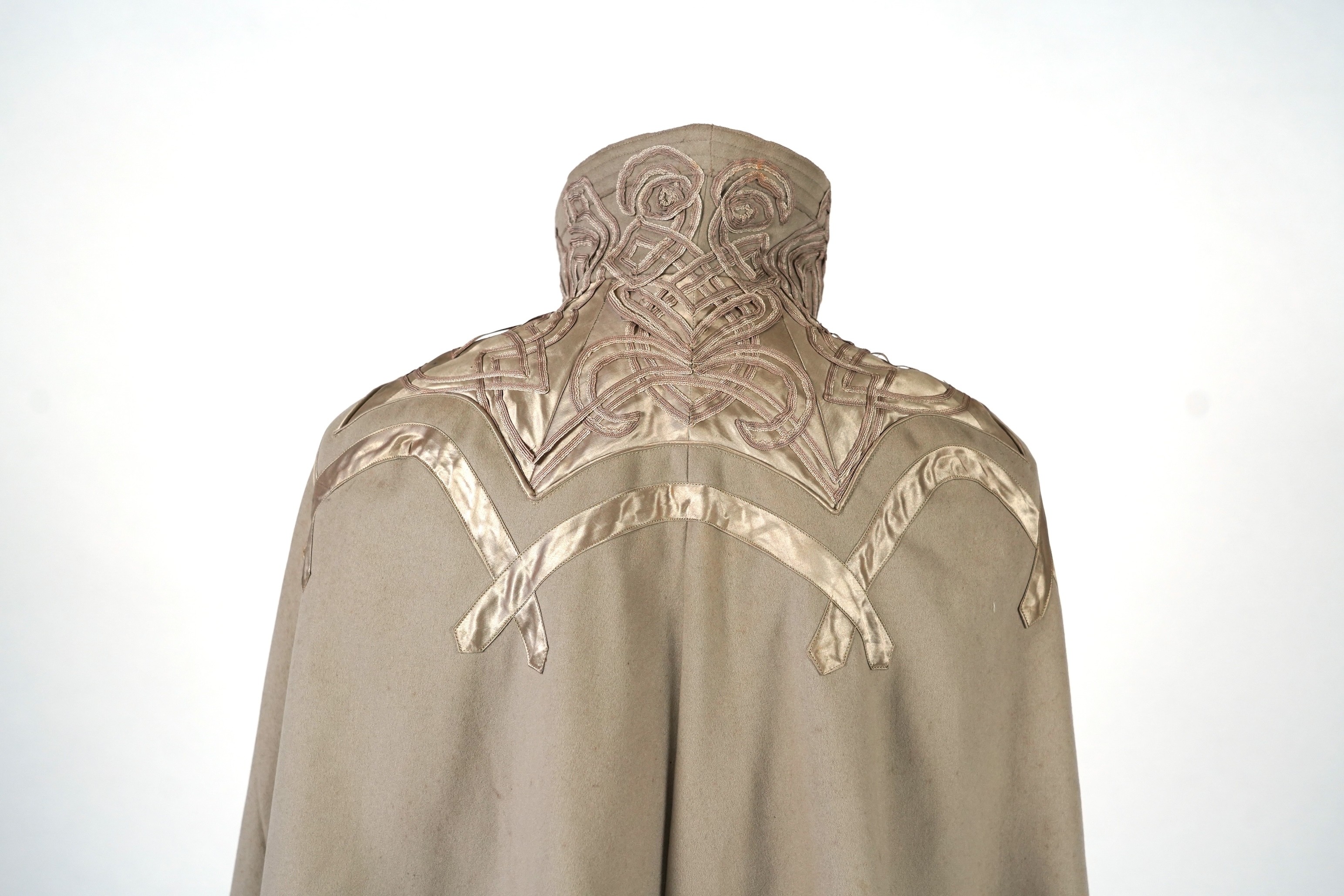 An Edwardian mushroom wool evening cape, decorated with silk ribbon worked strapping and ornate appliquéd fine braiding across the shoulders and under section of the collar, lined with cream silk satin.